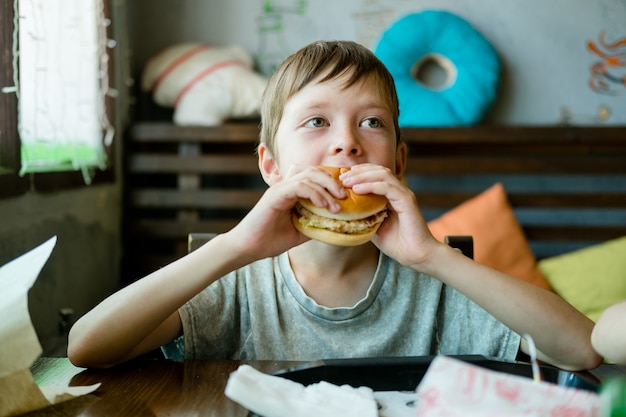 Boy eating a big burger with a cutlet. Hamburger in the hands of a child. Delicious and satisfying chicken cutlet burger. Takeout food