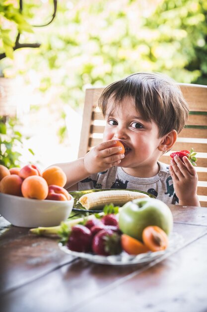 Photo a boy eating a green piece of fruit with a banana in his mouth