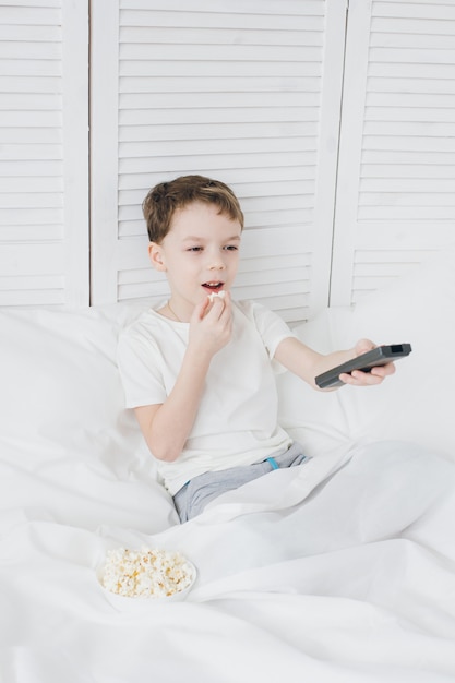 Boy eating popcorn sitting in bed and watching TV 