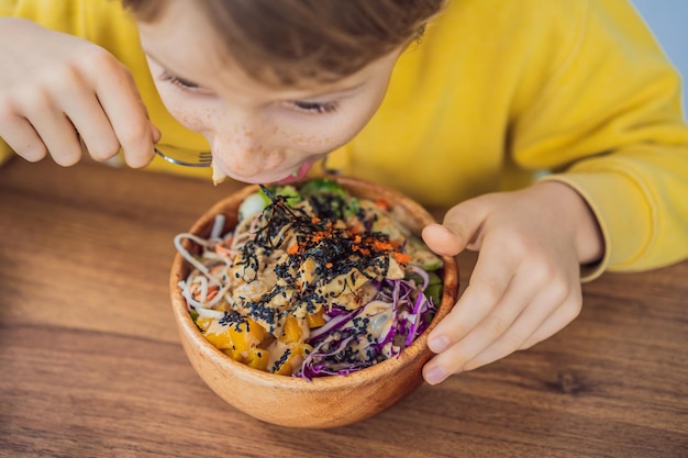 Boy eating raw organic poke bowl with rice and veggies closeup on the table top view from above