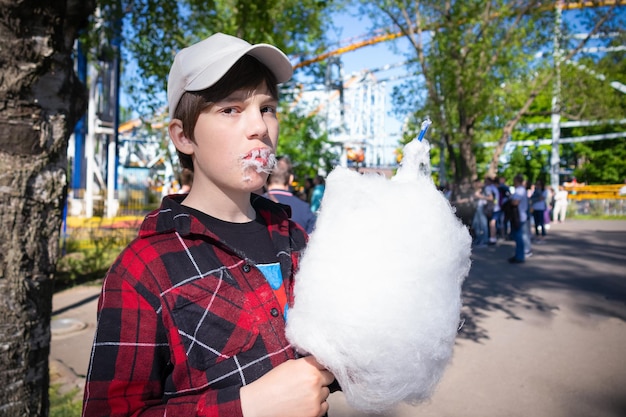 Boy eating white cotton candy in red plaid shirt and cap outdoor