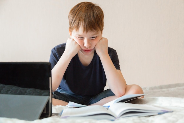 a boy of European appearance sits at home watching a computer A notebook is open in front of him