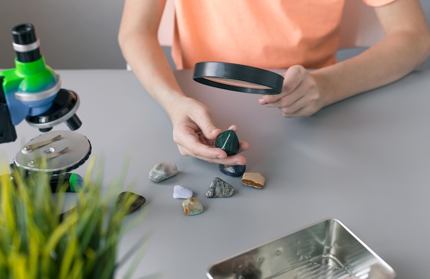 Boy examines semiprecious stones with magnifying glass on gray desk Children science concept