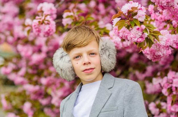 Boy fashionable teen posing near sakura. Confident stylish child enjoy warm spring day. Sakura garden concept. Child pink flowers of sakura tree background. Guy enjoying cherry blossom sakura.