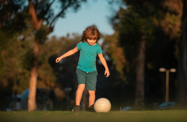 Photo boy football player kicking football on the sports field active kids child soccer player in park