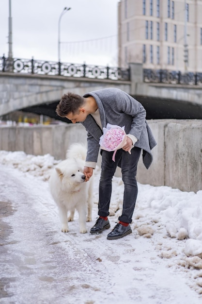 Boy friend with a bouquet of pink flowers hydrangea waiting for his girl friend outdoors while snow is falling. Valetnine`s day concept, wedding proposal. 
man goes on a date.