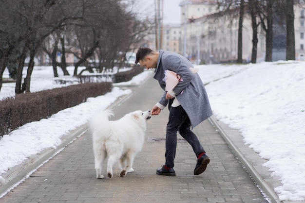 Boy friend with a bouquet of pink flowers hydrangea waiting for his girl friend and walking and playing with a dog. outdoors while snow is falling. Valetnine`s day concept, wedding proposal.
man goes