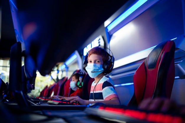 boy gamer wearing face mask and headset playing video games on computer in game room