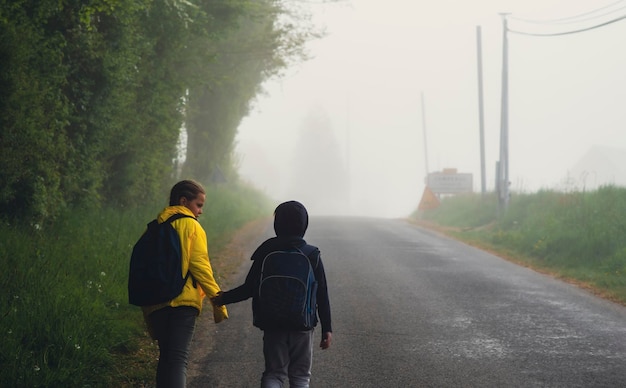 A boy and girl of 8 years old with a backpack goes to school along a country road in the morning alone in spring