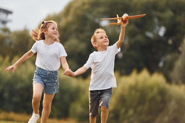 Boy and girl are playing with toy plane on the green field