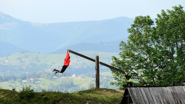 A boy and a girl are riding on a manual swing in the mountains