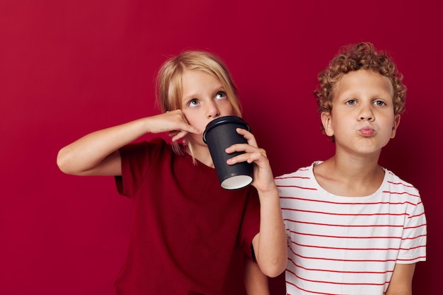 Boy and girl are standing next to a disposable glass with a drink red background