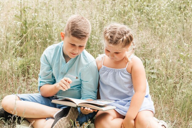 A boy and a girl, brother and sister read a book together in nature in the summer