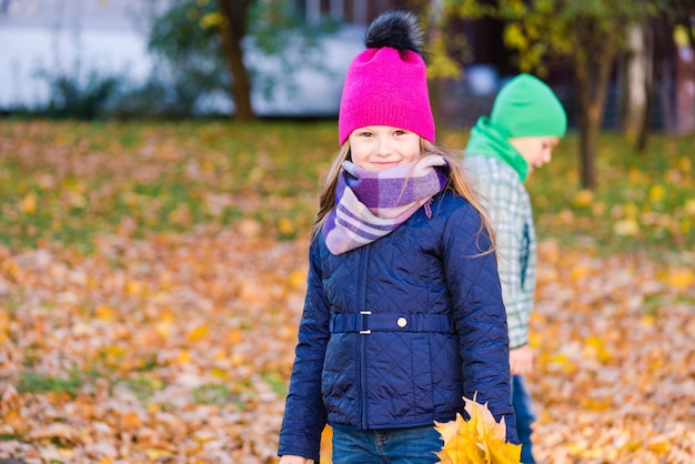 Boy and girl collect yellow maple foliage outdoors. Smiling girl looks into camera.