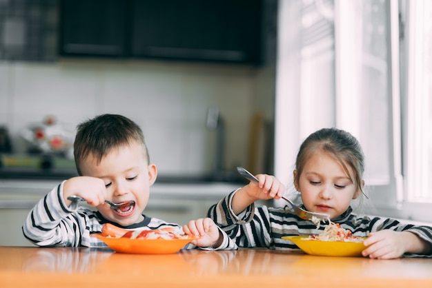 Boy and girl in the kitchen eating pasta