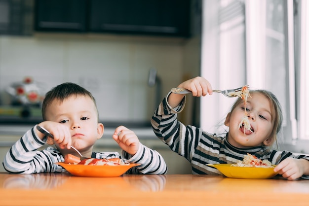 Boy and girl in the kitchen eating pasta