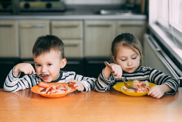 Boy and girl in the kitchen eating pasta