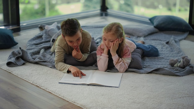 Boy girl lying on carpet with book Siblings looking for information in textbook