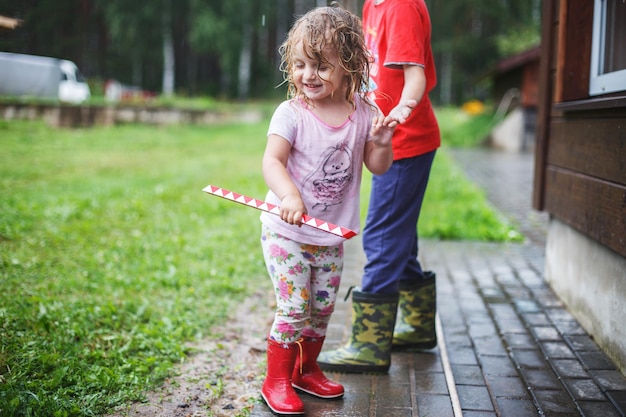 Boy and girl play in rainy summer park Children jump in puddle and mud in the rain