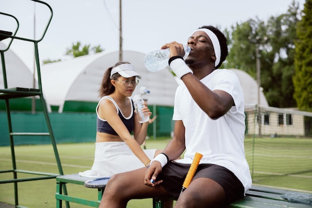 Boy and girl sit on bench near the tennis court during break in the tennis game