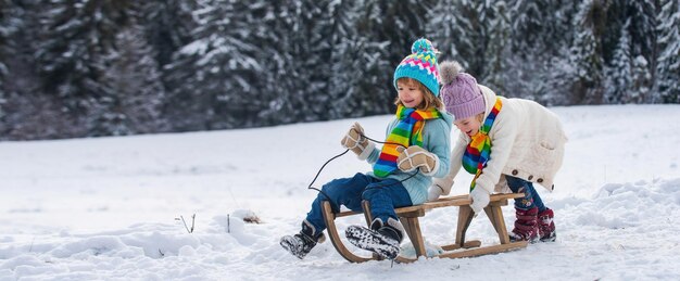 Boy and girl sledding in a snowy forest outdoor winter kids fun for christmas and new year children