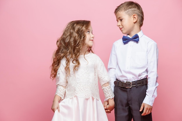 Boy and girl standing and posing in studio on pink background