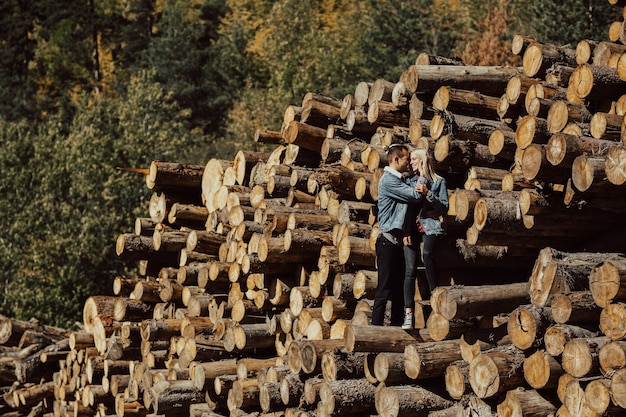 Boy and girl standing on the stack of firewood in the beautiful colorful autumn forest.