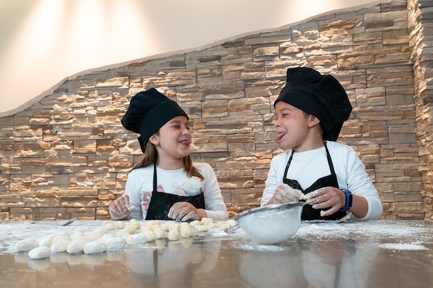 Boy and girl sticking out their tongues while doing a cooking workshop dressed as chefs