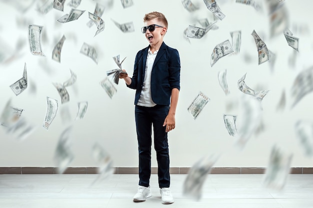 boy  glasses holds dollars and knows how to make money against the background of falling banknotes