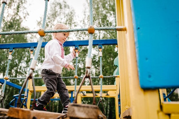 Boy go on the playground for children outdoors In an embroidered shirt Walking the stairs Close up take steps leg foot full length looking down