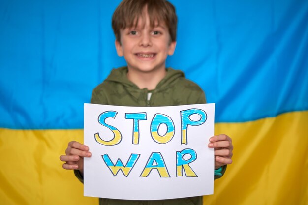 Boy hands holding yellowblue paper drawn stop war banner on Ukrainian flag background