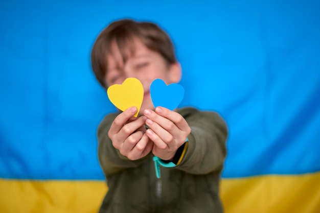 Boy hands holding yellowblue paperhearts on ukrainian flag background