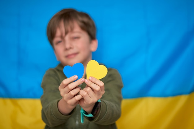 Boy hands holding yellowblue paperhearts on Ukrainian flag background