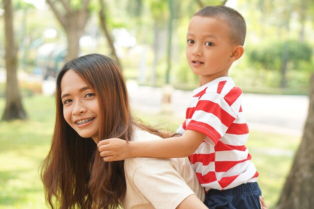 A boy happily rides on his mother's back in the park