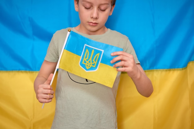 Boy holding in hands Ukrainian flag on yellowblue background Kids support Ukraine by showing heart Ukrainian crisis Russian aggression in Ukraine War of Russia against Ukraine