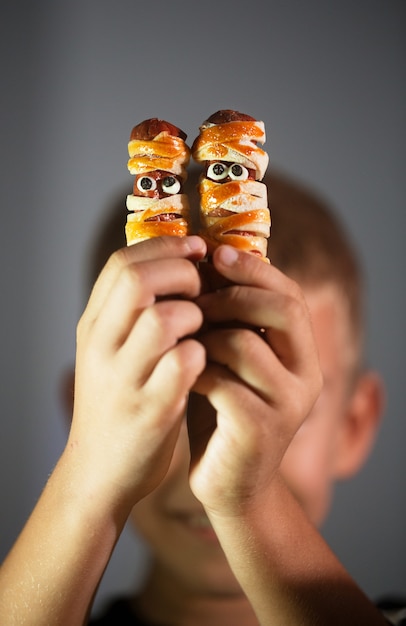 Boy holds mummy shaped Halloween snacks made from dough and sausage