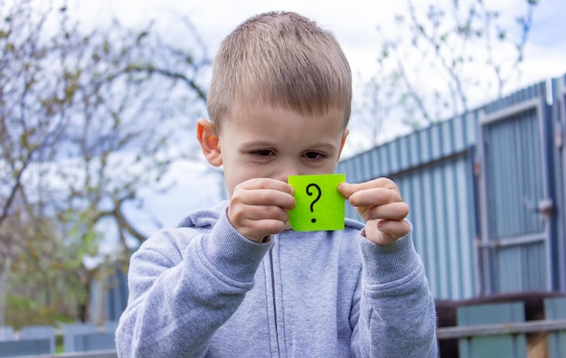 The boy holds stickers with a question mark on the background of the park Nature