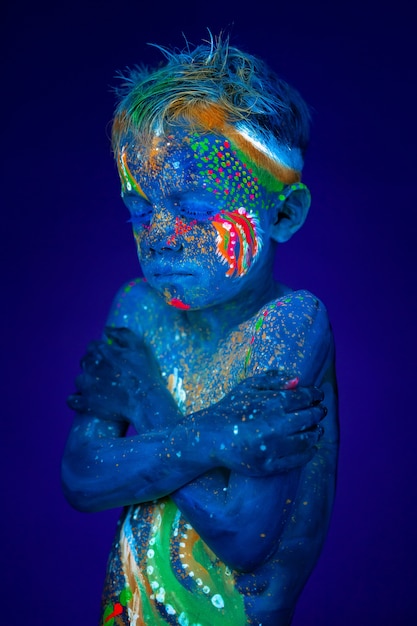 Boy hugs himself, he is very cold. Posing in UV ultraviolet light