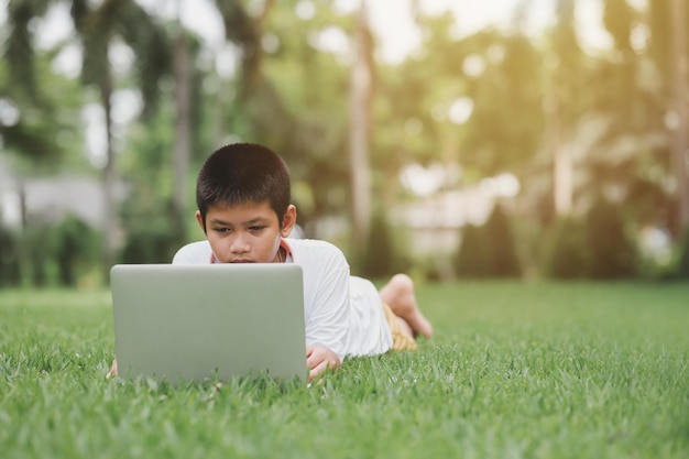 Boy interested in studying online on a notebook computer on the green grass in the park