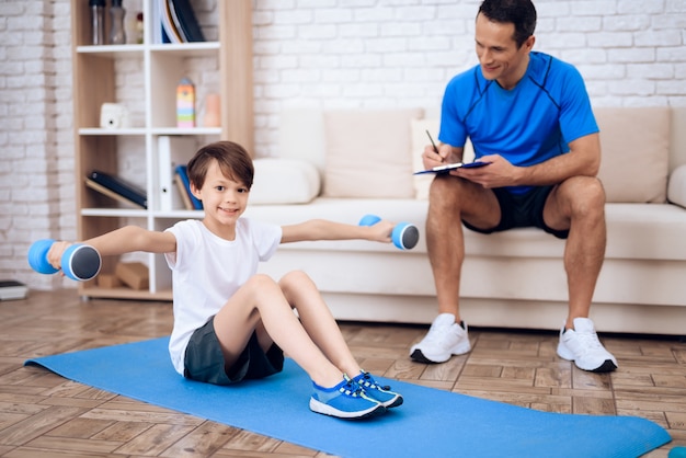 A boy is doing exercises with dumbbells on the floor.