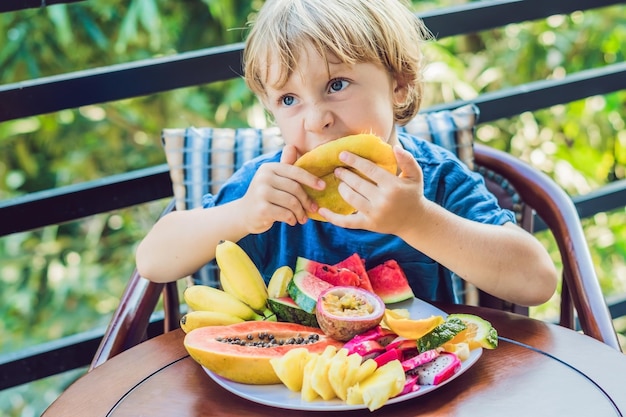 The boy is eating different fruits on the terrace.