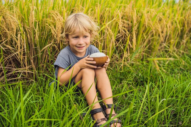 Boy is holding a cup of boiled rice in a wooden cup on the background of a ripe rice field food for