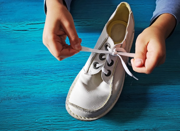 Boy is learning how to tie shoelaces, close-up on the hands and the shoe