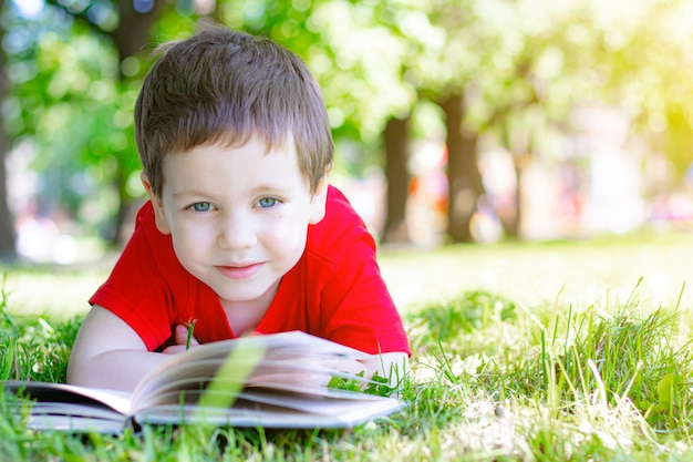 The boy is lying on the grass and reading a book. Reading in nature.