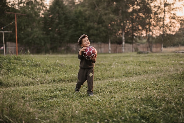 A boy is playing football in the countryside The joyful childhood of the baby Active sports