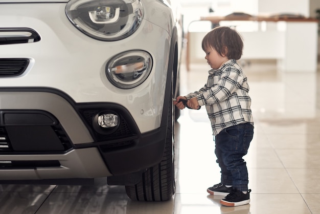 The boy is playing near the car that his parents just bought.