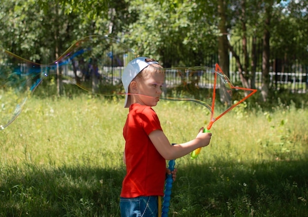 A boy is playing with huge soap bubbles in the park Summer holidays active lifestyle Cheerful charming child enjoys healthy summer outdoor play