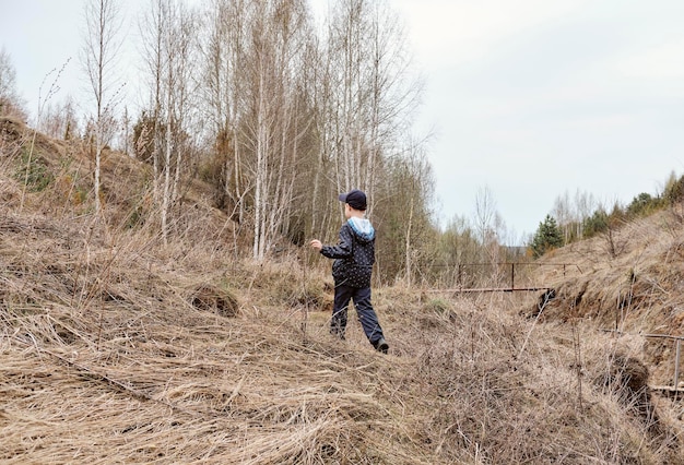 Boy is running down from the hill on a cloudy autumn day A hill with dry grass sandy path childhood in countryside Lonely boy playing