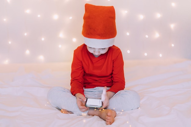 The boy is sitting in the phone on the background of a garland New Year and Christmas Festive mood