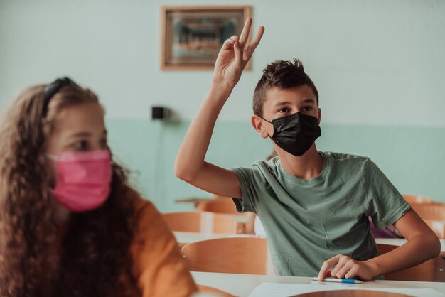 The boy is sitting at a school desk and wearing a mask on his face against corona virus protection New normal Education during the Covid19 pandemic Selective focusHigh quality photo